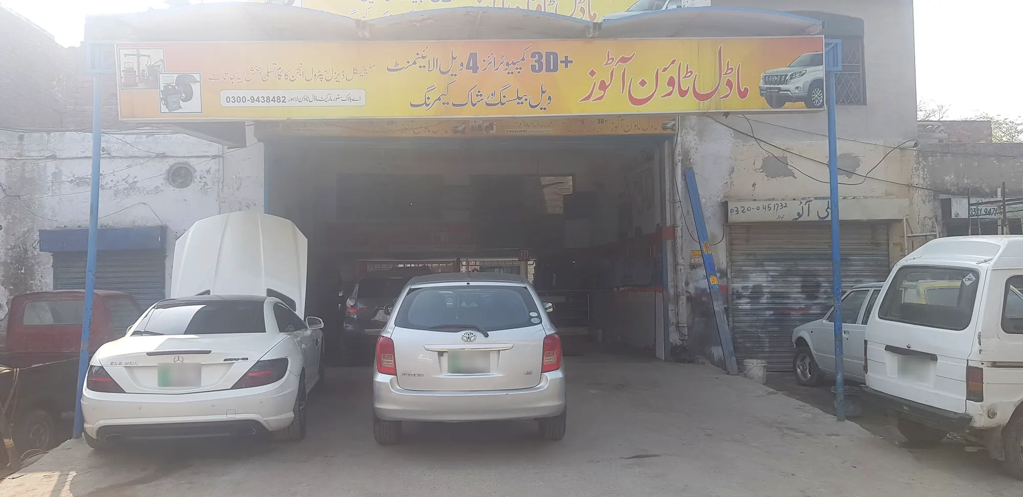 The front of the Model Town Autos bay with the yellow board, a sports car with its bonnet up and a Corolla on the ramp